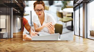 Cafe coworking: Two women discussing work on a laptop Wall mural