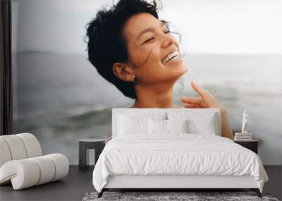 Carefree woman with wavy hair posing joyfully by the seaside beach Wall mural