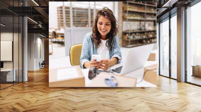 Cheerful online store owner reading a text message on her smartphone Wall mural