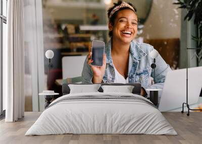 Cheerful woman recommending a mobile app at a coffee shop Wall mural