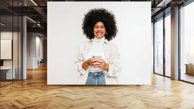 Cheerful young woman smiling at the camera while holding a smartphone Wall mural