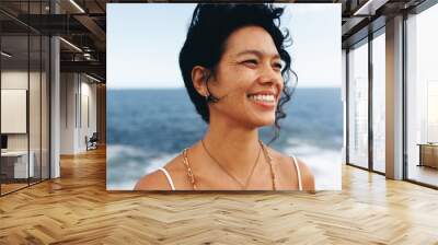 Close-up of smiling woman with wavy hair and bohemian jewelry at the seaside Wall mural