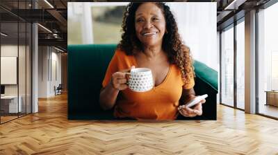 Elderly woman holding a smartphone as she enjoys a warm cup of coffee Wall mural