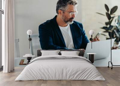 Focused businessman using laptop and smartphone in office Wall mural