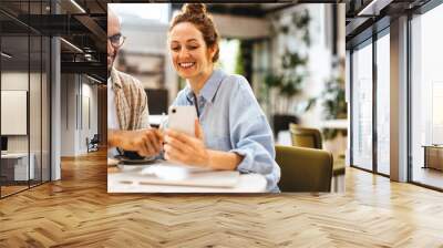 Happy colleagues using a mobile phone while working together in a cafe Wall mural