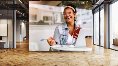 Happy female student sitting in a coffee shop, using a smartphone Wall mural