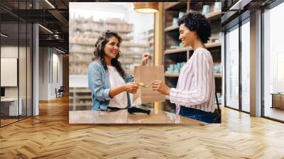 Happy young shop owner receiving a credit card from a customer Wall mural