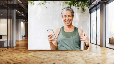 Motivated senior woman browsing some music for her outdoor workout routine Wall mural