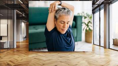 Overhead tricep stretch during yoga: Senior woman doing an arm exercise at home Wall mural