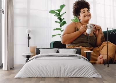 Smiling woman sitting on sofa having coffee Wall mural