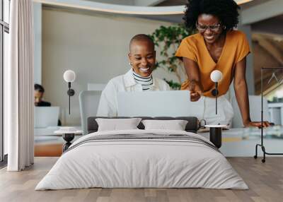 Two businesswomen collaborating on laptop in office Wall mural