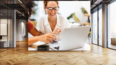 Two happy women using a laptop to brainstorm in a coworking space Wall mural