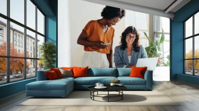 Two professional women collaborating happily over laptop in modern office Wall mural