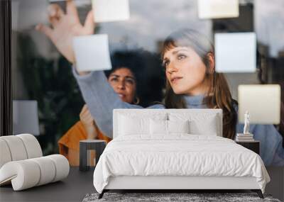 Two young businesswomen brainstorming using adhesive notes in an office Wall mural