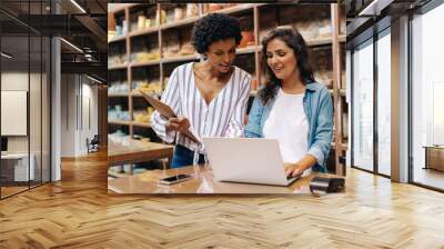 Two young shop owners using a laptop in their store Wall mural