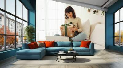 Woman sitting on bed with christmas presents doing a video call Wall mural