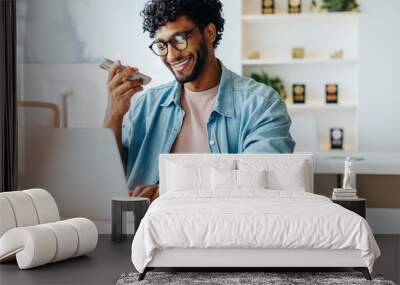 Young businessman using smartphone and laptop at office desk Wall mural