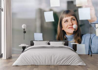 Young female entrepreneur sticking adhesive notes to a glass wall Wall mural