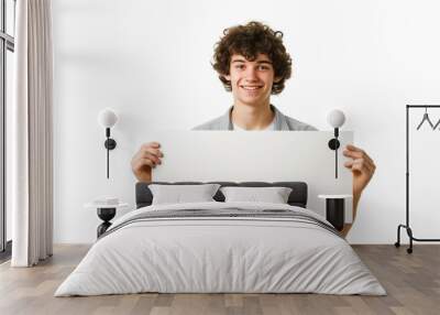 smiling young man with curly hairstyle holds empty white rectangular banner, isolated on white background Wall mural