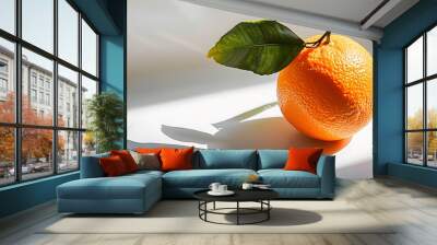 A ripe orange with a smooth peel and a green leaf attached placed on a pristine white surface casting a soft shadow Wall mural