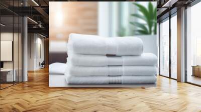 Elegant white towels neatly arranged on a white wooden table, featuring a serene blurred plant background that enhances the calming atmosphere . Wall mural