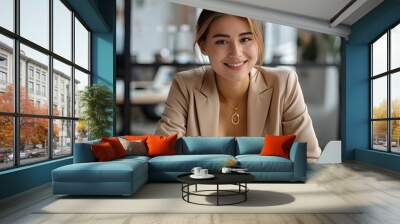 A photo of a young professional woman sitting at her desk and smiling at the camera. She is wearing a suit jacket and has her hair in a bun. She is surrounded by papers and files. Wall mural