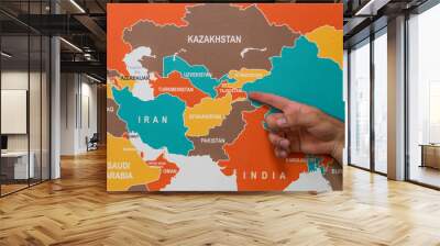 A hand pointing to Tajikistan on a wall map indicating the geographical location and the concept of popular tourist destination and travel.	 Wall mural