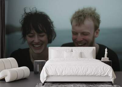 A candid shot of a young couple laughing together outdoors, their carefree expressions capturing a moment of joy and connection in a moody, natural setting. Wall mural