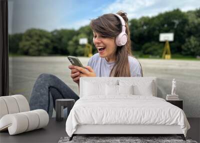 Young woman with headphones looking at her cell phone with surprised expression 
 Wall mural