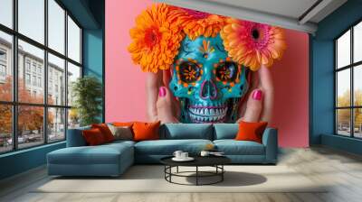 Hands holding a colorful Mexican skull adorned with orange flowers against a pink background with space for text. Banner, web, or advertisement about Día de Muertos and Mexican culture and tradition. Wall mural