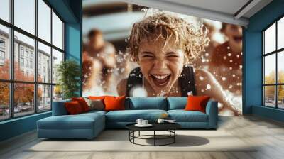 A boy laughs heartily while splashing water with friends at the beach, captured in an exuberant moment of joy and play, with a yacht in the background adding to the scene's vibrancy. Wall mural