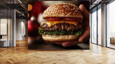 A close-up of a delicious cheeseburger with sesame seed bun, fresh tomatoes, crisp lettuce, and melted cheese held in hand with festive lights in the background. Wall mural