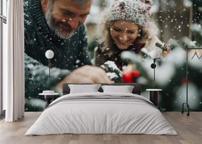 A festive Christmas tree is being decorated outdoors as snow falls, capturing the joyful and cozy holiday spirit amid a wintery wonderland. Wall mural