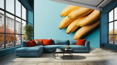 A handful of vibrant, ripe yellow bananas set against a blue background, highlighting their freshness and tropical appeal, making them a delightful, healthy snack. Wall mural