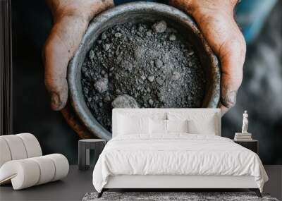 A pair of hands, with dirt-covered fingers, hold a bowl filled with dark grey soil, depicting a sense of connection to the earth and the raw and elemental nature of this natural substance. Wall mural