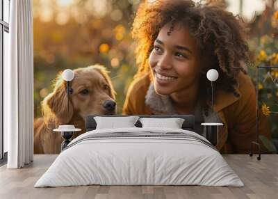 A woman with curly hair dressed in casual autumn attire is outdoors with her loving golden dog, illustrating a joyful moment of companionship in nature. Wall mural