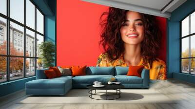 A woman with curly hair poses elegantly against a red background, exuding confidence and charm in a modern fashion setting, captured perfectly with style. Wall mural