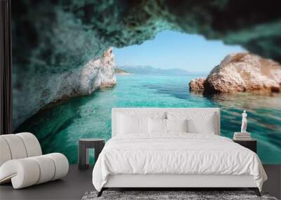 Stunning view of the turquoise sea through the entrance of a rocky cave, with clear blue skies and distant mountains seen in the background, exemplifying natural beauty. Wall mural