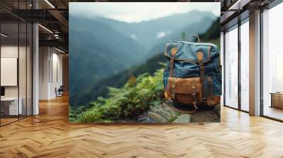 A blue and brown backpack placed on a mountain trail, with lush greenery and cloudy skies in the background, illustrating the essence of hiking and adventure. Wall mural