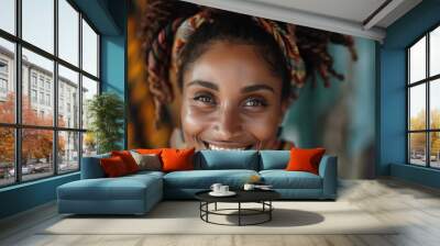 A radiant woman with a colorful headwrap and wooden earrings is seen smiling broadly, standing against a background filled with vibrant fabrics, exuding happiness and energy. Wall mural