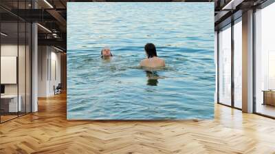 Two girls swim in the river in the evening in turquoise water Wall mural