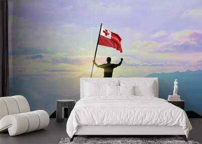 Tonga flag being waved by a man celebrating success at the top of a mountain against sunset or sunrise. Tonga flag for Independence Day. Wall mural