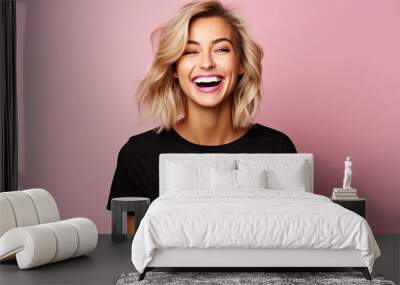 a beautiful blonde woman wearing black shirt expressing happiness emotion with her mouth laughing and big wide open eyes. isolated on pink background Wall mural