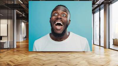 Portrait of a happy and excited man looking up with mouth open on pastel blue background Wall mural