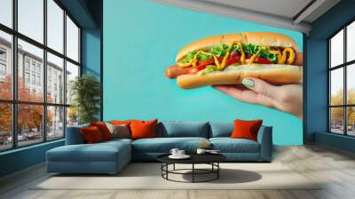 Woman hand holding delicious hot dog , on pastel blue background Wall mural