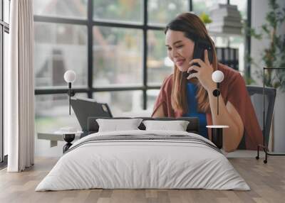 Businesswoman smiling while talking on the phone and working on a digital tablet, demonstrating efficiency and connectivity in a modern office setting Wall mural