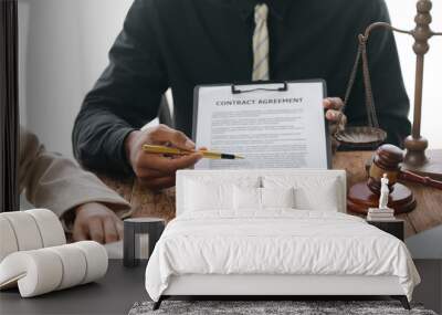 Lawyer is explaining a contract agreement to clients and pointing with a pen during a meeting at a table with a gavel and scales of justice Wall mural