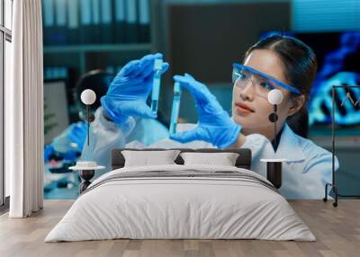 Scientist wearing a lab coat and protective goggles is carefully comparing the contents of two test tubes in a laboratory Wall mural