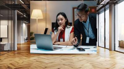 two asian business people working late together in office using laptop computer and analyzing financ Wall mural