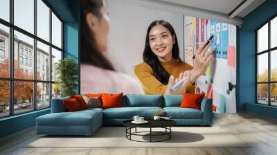 Two asian women working as uiux designers and discussing over mobile app interface wireframe design in office Wall mural